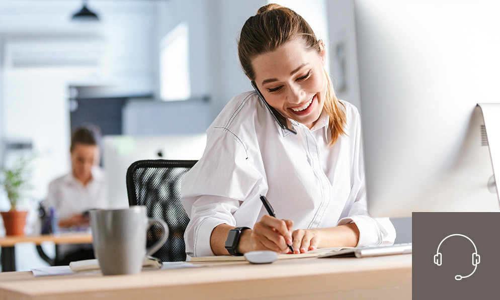 Mitarbeiterin im Büro telefoniert und macht sich Notizen am Computer – freundliche Beratung und professionelle Projektabwicklung im Bereich Objektausstattung durch WESPRO Hospitality.
